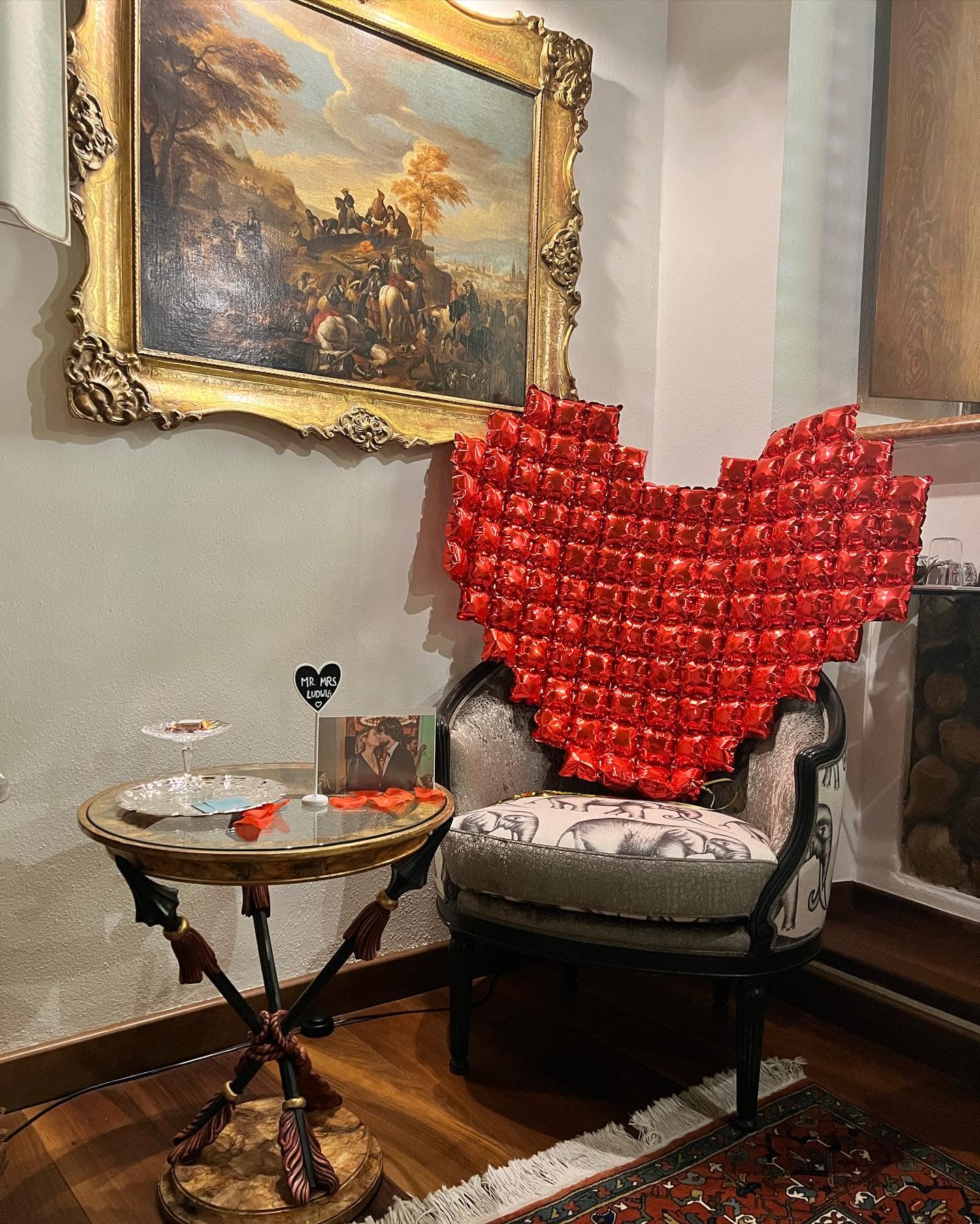 Allestimento romantico nella suite Marcello a Verona: cuore di rose rosse sulla poltrona d’epoca, tavolino con biglietto e quadro del Settecento