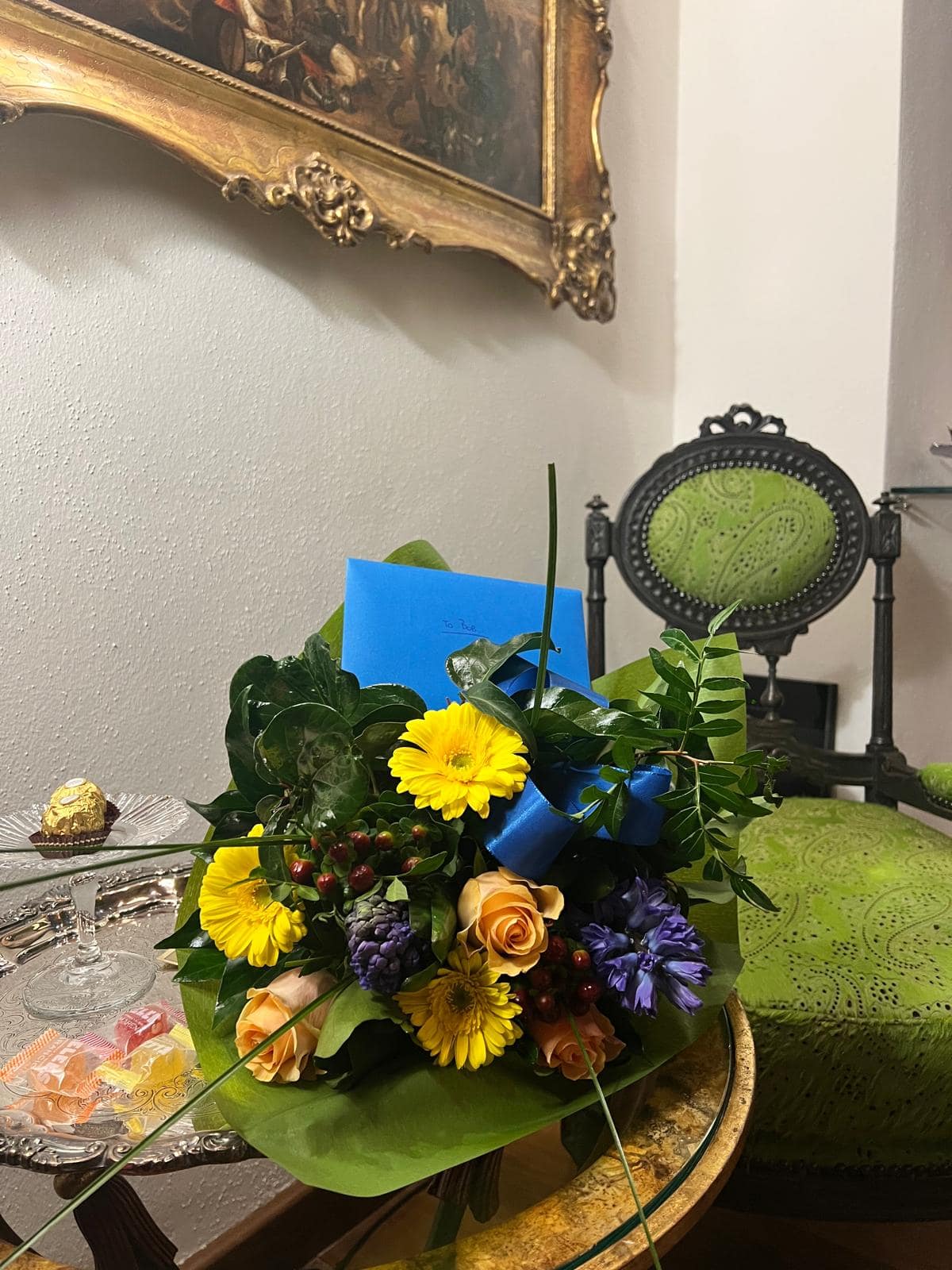 Bouquet di fiori colorati con biglietto d’auguri e cioccolatini nella suite Marcello a Verona, allestimento di benvenuto sulla poltrona d’epoca verde