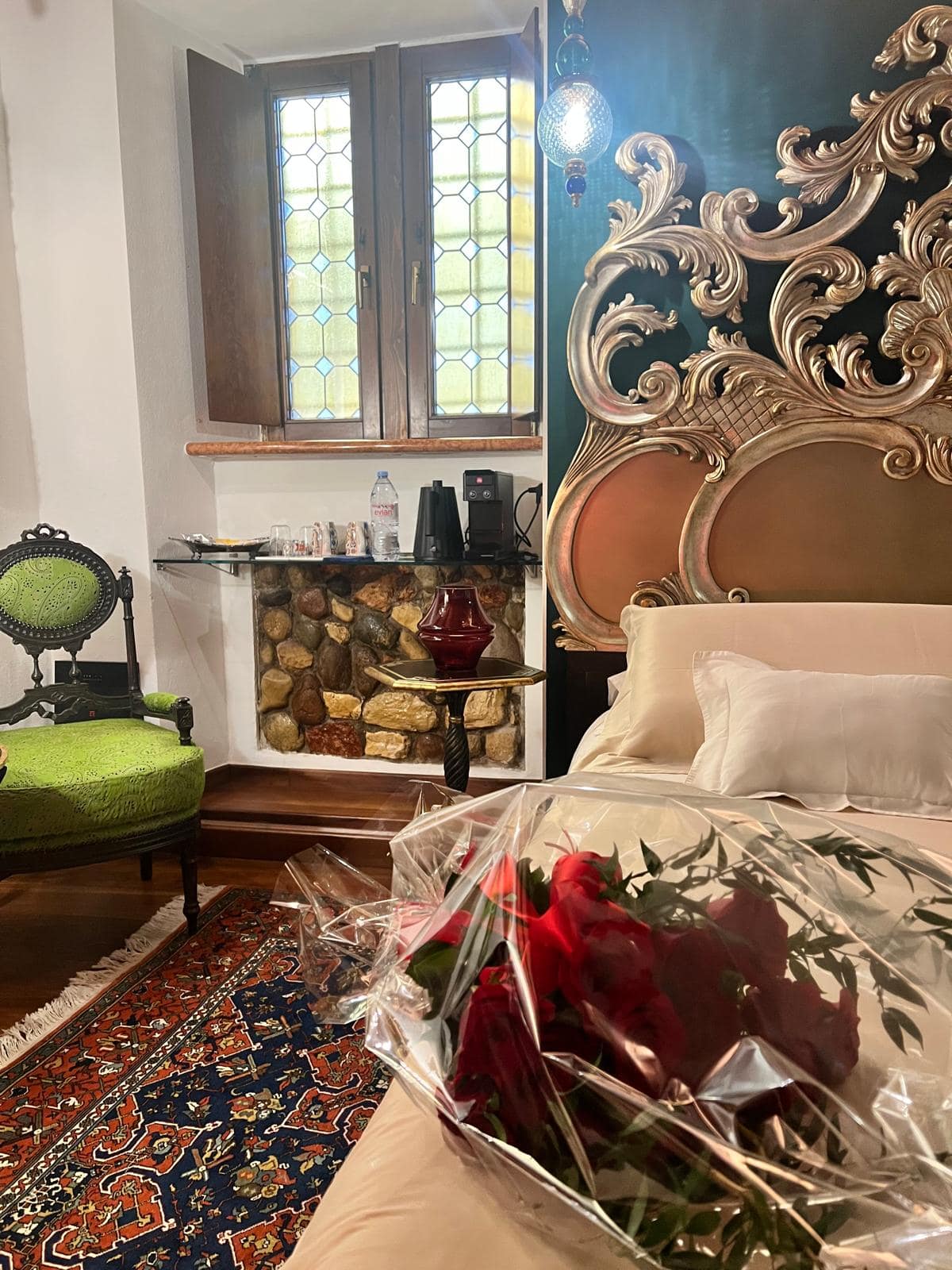 Camera della suite Marcello a Verona con testiera barocca dorata, mazzo di rose rosse sul letto e poltrona d’epoca, allestimento romantico