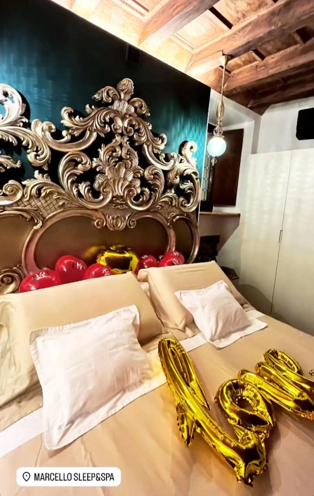Letto matrimoniale con testiera barocca dorata addobbato con palloncini a cuore rossi e scritta dorata nella suite Marcello a Verona, sorpresa per occasione speciale