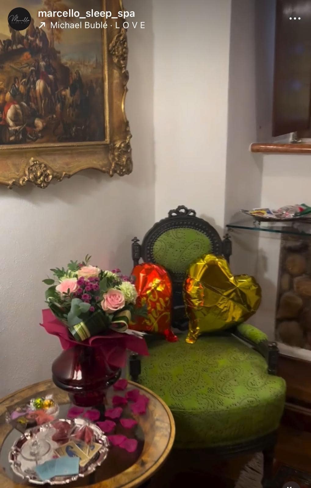 Allestimento romantico al Marcello Sleep & Spa di Verona: palloncini a cuore rosso e oro, bouquet di rose rosa e petali con cioccolatini sulla poltrona d’epoca