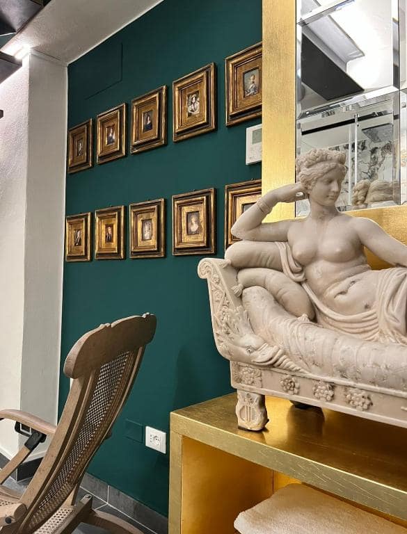 Zona relax della SPA Marcello a Verona: parete verde smeraldo con galleria di miniature antiche in cornice dorata e statua di Venere reclinata in marmo bianco su console dorata