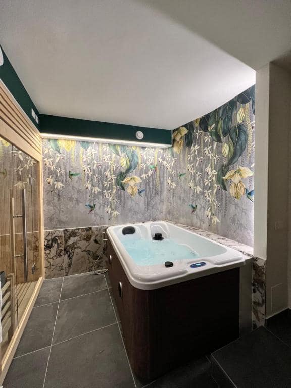 Vasca idromassaggio rettangolare della SPA privata Marcello a Verona, con carta da parati botanica decorata da foglie verdi-gialle, fiori bianchi e colibrì, sotto soffitto verde scuro