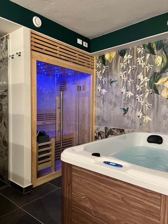 Vista laterale del piano −1 della SPA Marcello a Verona: vasca idromassaggio in primo piano, sauna finlandese in luce blu sullo sfondo e doccia in marmo a sinistra