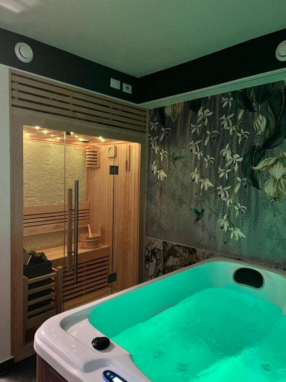SPA privata Marcello a Verona in cromoterapia verde acqua: vasca idromassaggio in primo piano, soffitto in tinta e carta da parati botanica scura