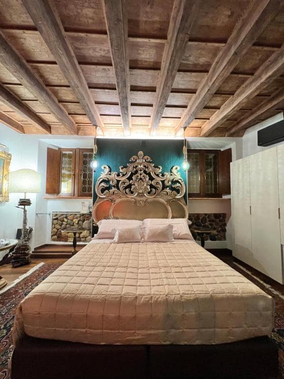 Vista frontale ampia della suite Marcello a Verona: letto matrimoniale, testiera barocca argentata, parete turchese, armadi del Settecento ai lati e soffitto a travi a vista