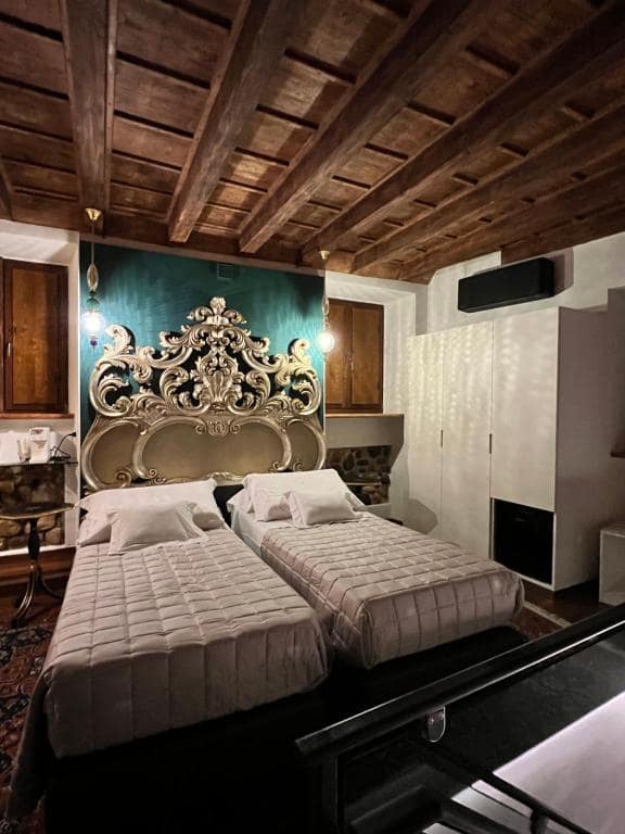 Suite Marcello a Verona in configurazione twin vista dall’alto della scala: due letti singoli condividono la testiera barocca dorata, parete verde smeraldo e soffitto a travi a vista