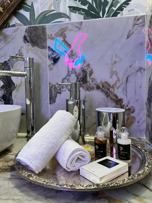 Vassoio in argento decorato nella SPA Marcello a Verona: asciugamani bianchi arrotolati, dispenser sapone in argento e BB Cream italiana in omaggio; sullo sfondo marmo Calacatta viola e insegna al neon a forma di mani intrecciate