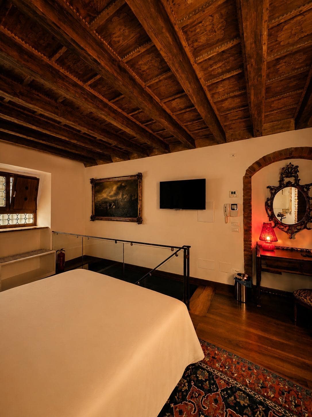 Altillo de la suite Marcello en Verona: óleo paisajístico del siglo XVIII en marco dorado junto a la Smart TV con acceso gratuito a Netflix, barandilla de cristal y techo con vigas vistas