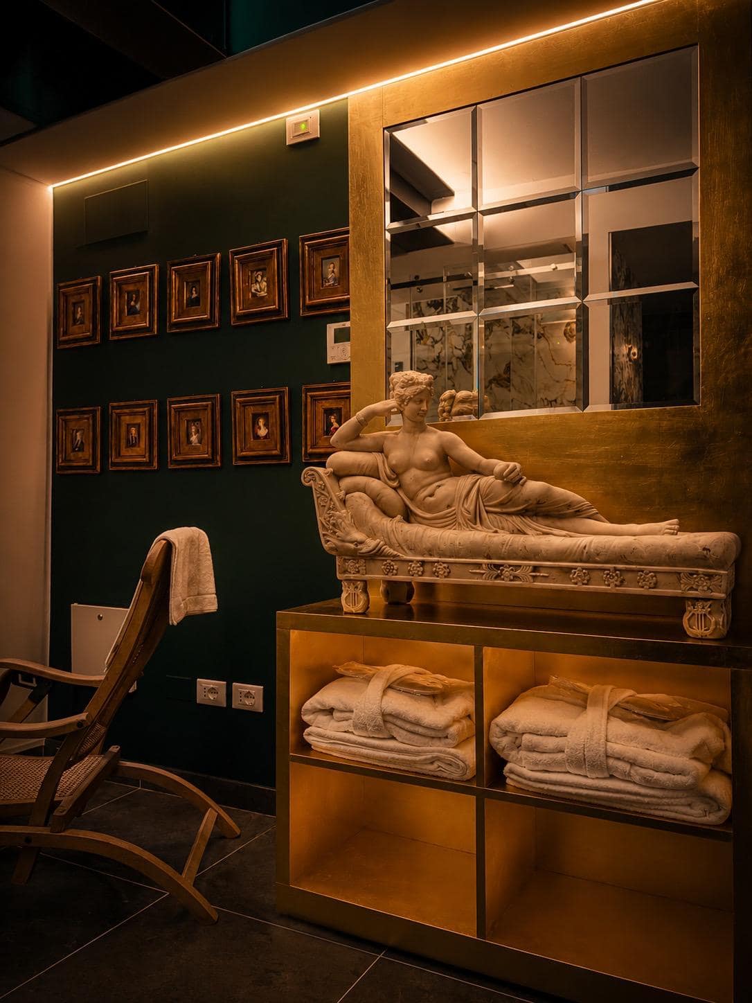Estatua de Venus reclinada en mármol blanco sobre consola dorada en el spa Marcello en Verona, ante la pared verde esmeralda con galería de miniaturas antiguas en marcos dorados