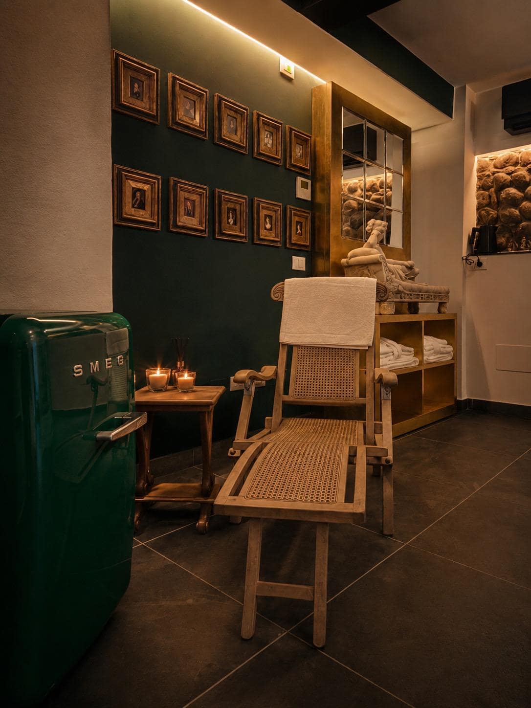 Zona de relax del spa privado Marcello en Verona: tumbona acolchada, nevera Smeg verde retro y pared verde esmeralda con galería de miniaturas en marcos dorados